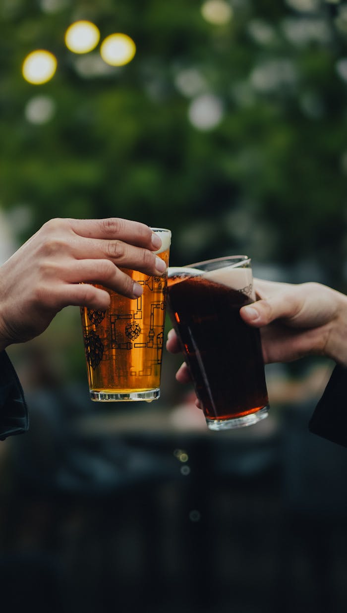 Two people toasting with beer glasses outdoors during the day, celebrating togetherness.