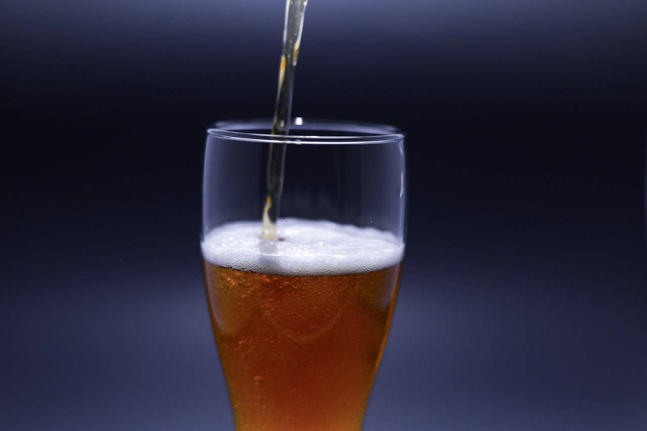 Detailed close-up of golden beer being poured into a glass, isolated on a dark background.